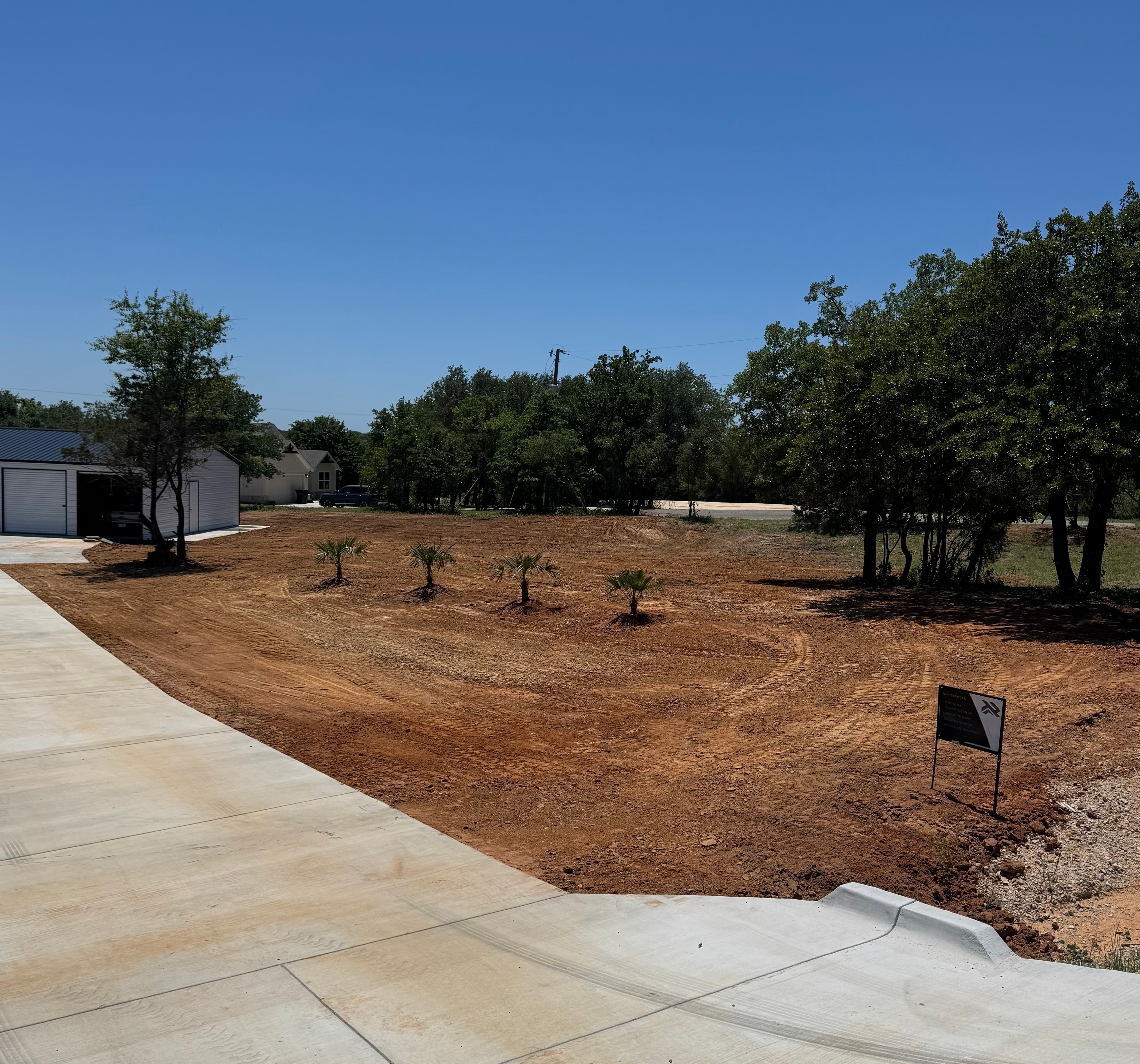Finished concrete driveway with freshly graded yard and metal building